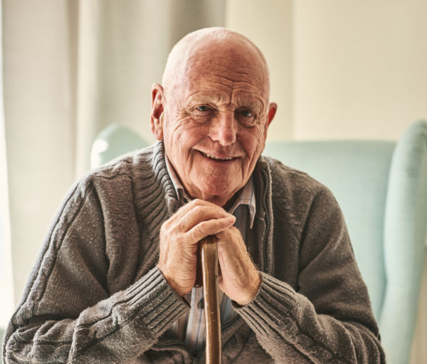 elder man sitting on couch in his home holding a cane