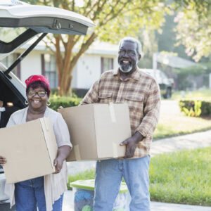 A senior African-American couple relocating, moving to a new home. They are excited, unloading boxes from their car. They are in their 70s, downsizing in retirement.